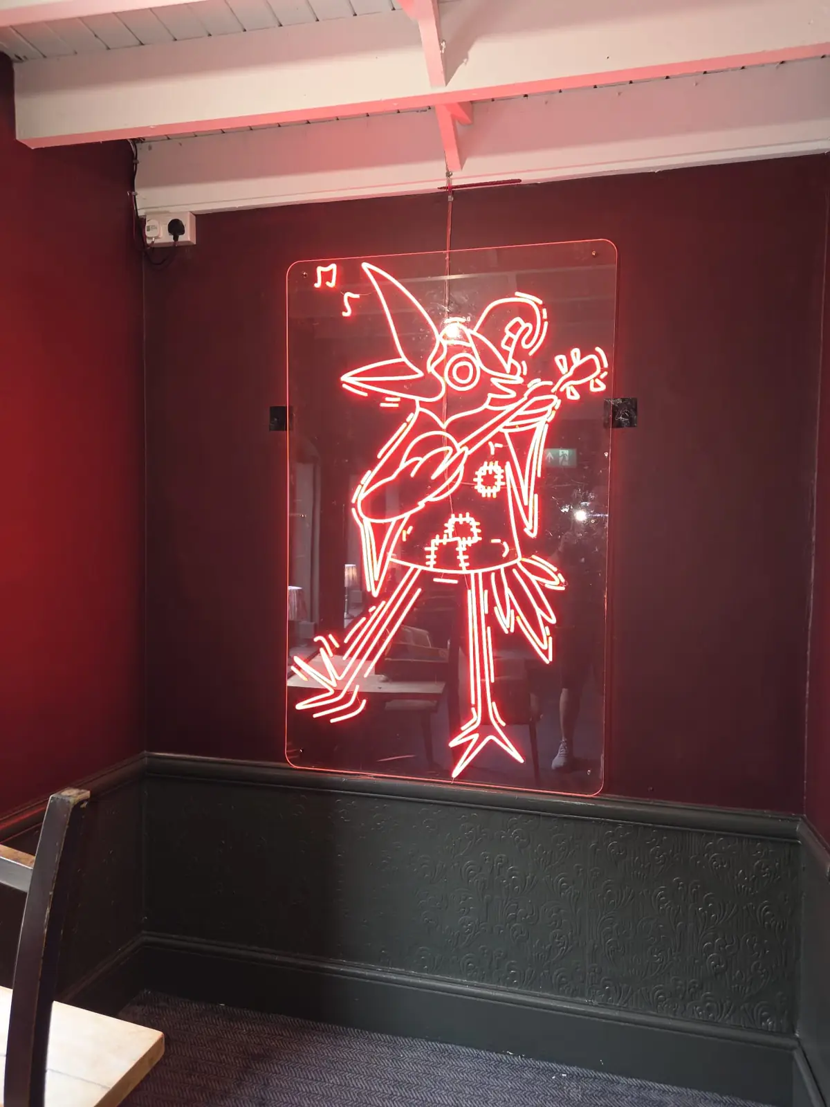 A red neon sign of a bird playing a guitar on an oxblood wall