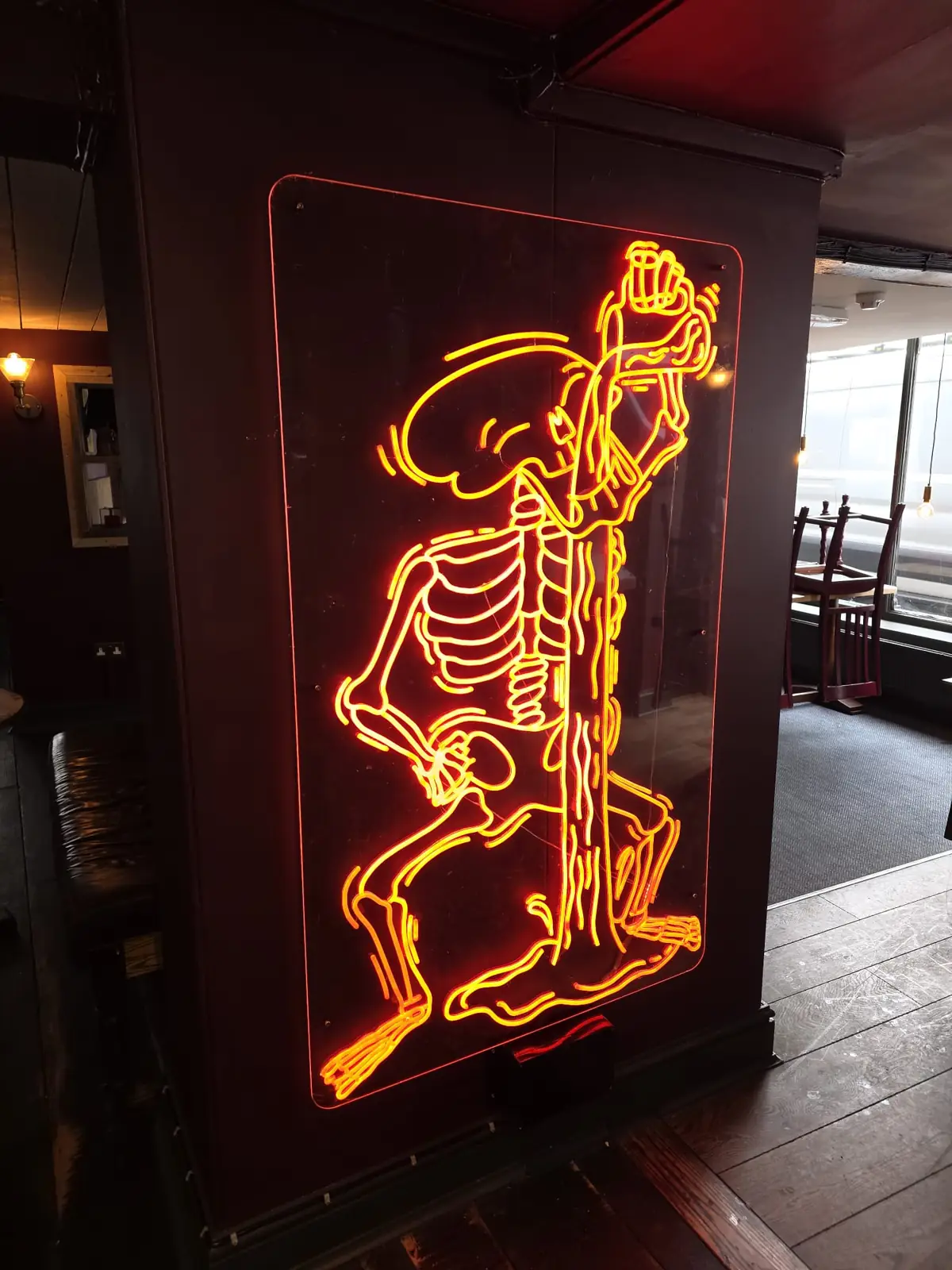 An orange neon skeleton downing a drink, glowing on a black pillar