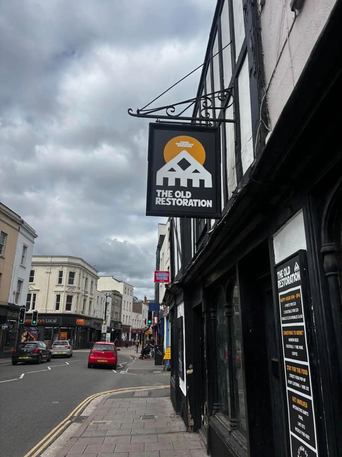 The pub's hanging sign: an orange sun behind a white roofline, with The Old Restoration lettered underneath